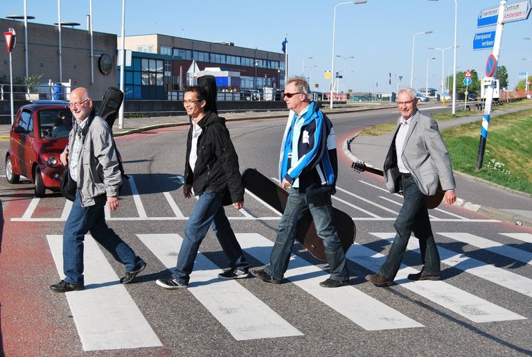 De vier bandleden lopen met hun instrumenten over een zebrapad